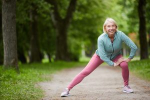 Woman on trail stretching before a run, for ways to improve your body's health with exercise call Chiropractor Office Munster.