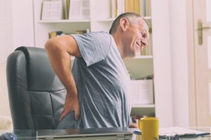 Man with lower back pain while sitting at desk at work, representing Back Pain Treatment Highland.