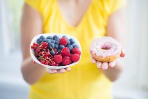 Woman holding bowl of berries and donut in other hand, for Chronic Pain Management St. John change to healthy diet.