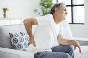 Senior man with back pain sitting on couch, concept for Back Pain Treatments in Winfield IN.